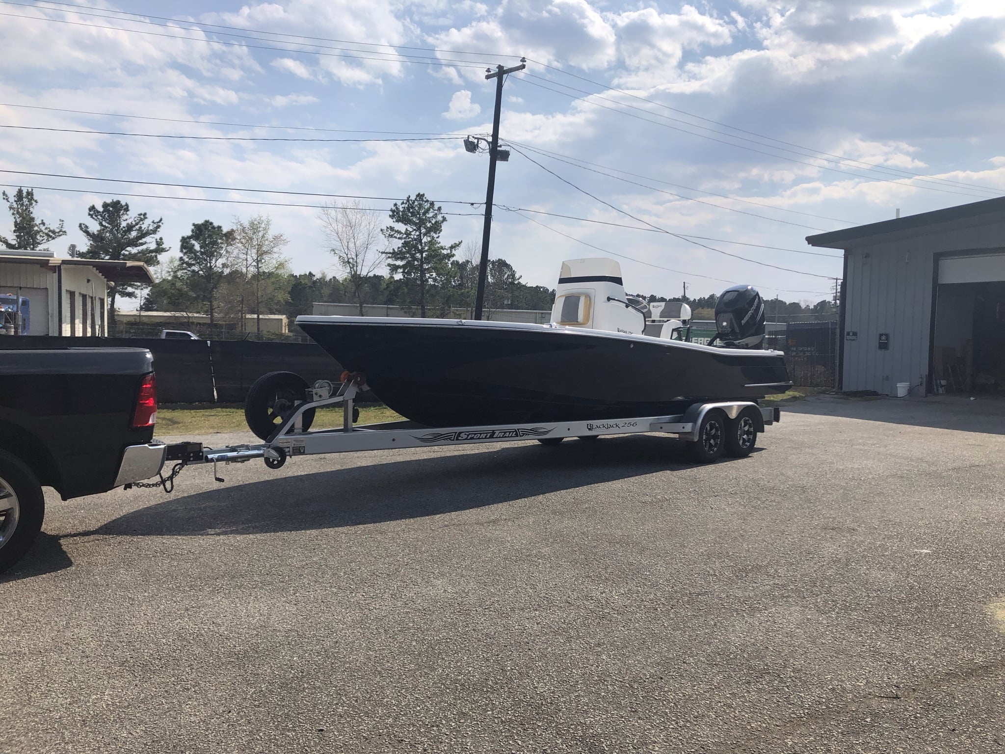 A matte black boat on a trailer hitched to a pickup truck in a parking lot.