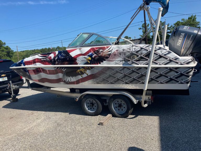 A boat on a trailer wrapped in a bald eagle and American flag graphic under a blue sky.