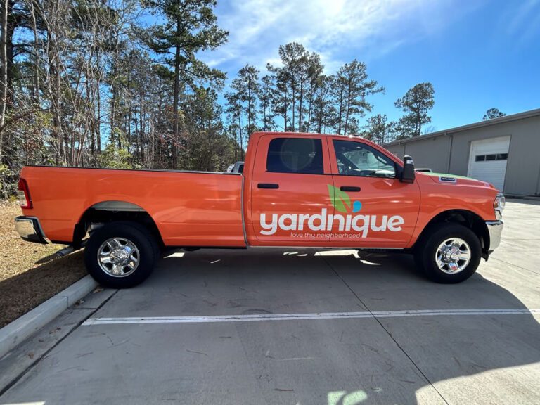 An orange pickup truck displays the Yardnique landscaping logo and tagline on its door and bed.