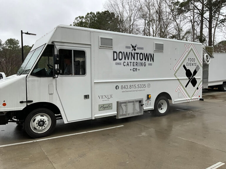 A white step van wrapped for Downtown Catering Co. with contact details, parked on a wet lot.