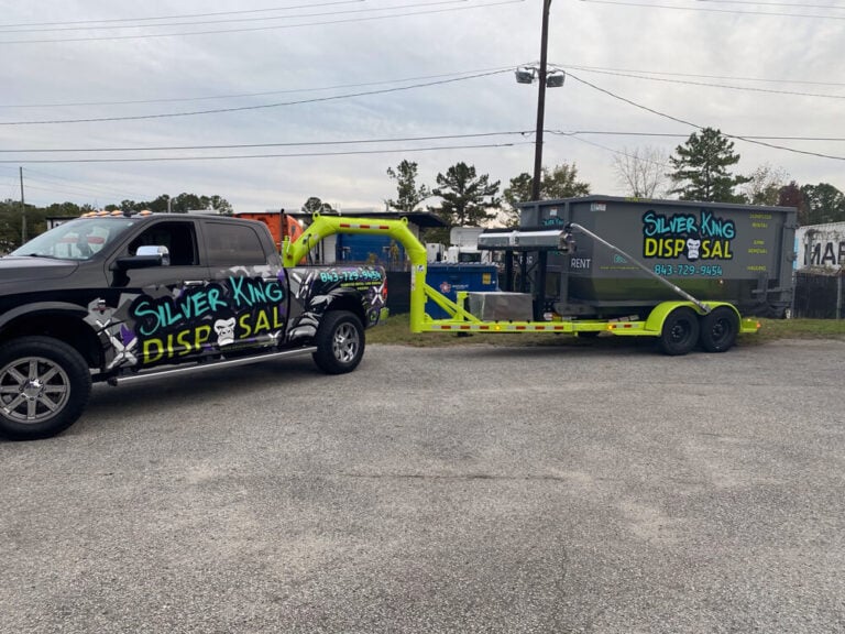 A black pickup truck and matching dumpster trailer wrapped in bold green and purple Silver King Disposal graphics.