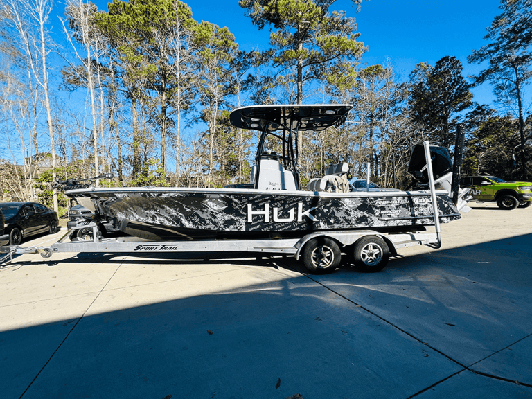 A center console boat on a trailer displays a black and white camouflage Huk wrap with sponsor logos.