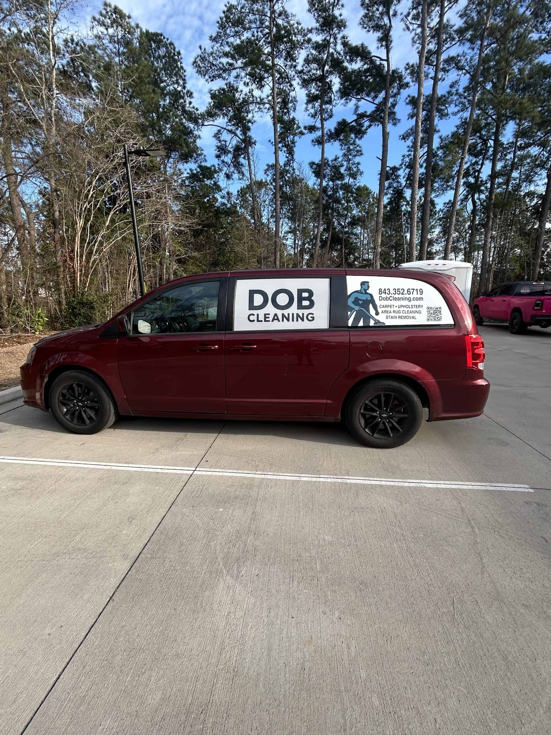 A dark red minivan wrapped with DOB Cleaning branding and service details, parked among pine trees.