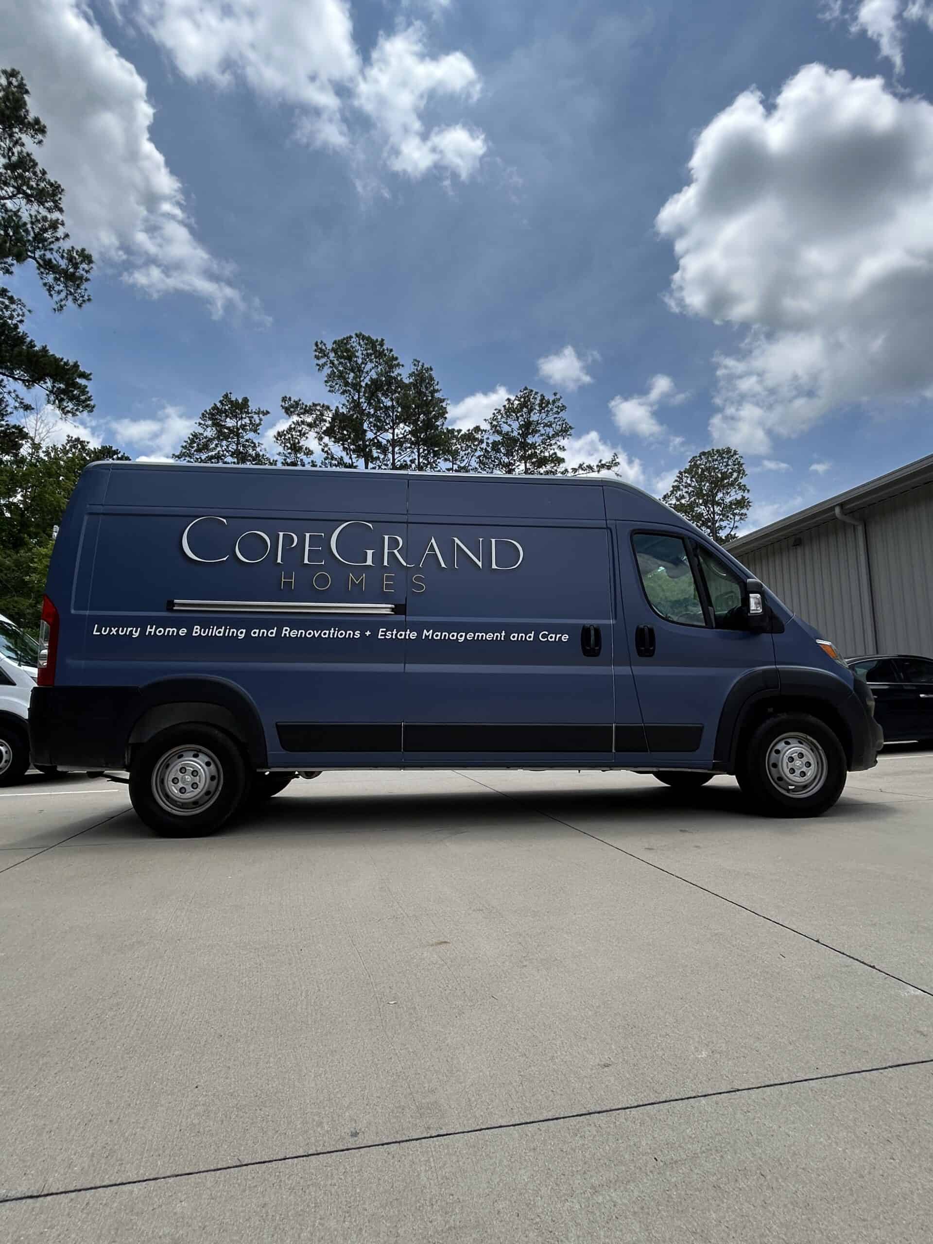 A navy blue cargo van with a CopeGrand Homes wrap parked beneath a partly cloudy sky.