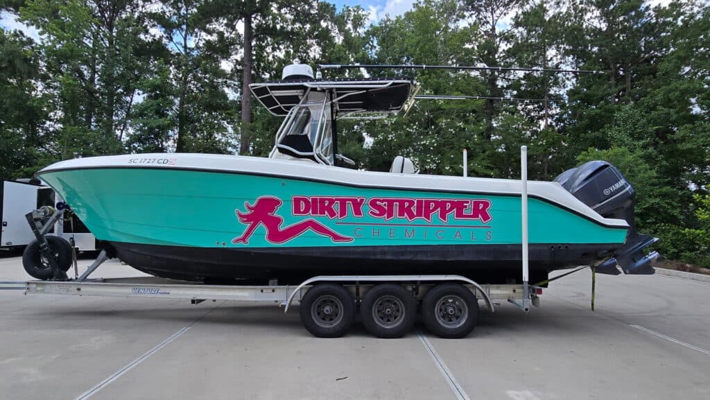 A teal and white center console boat on a trailer displays a Dirty Stripper Chemicals logo wrap.