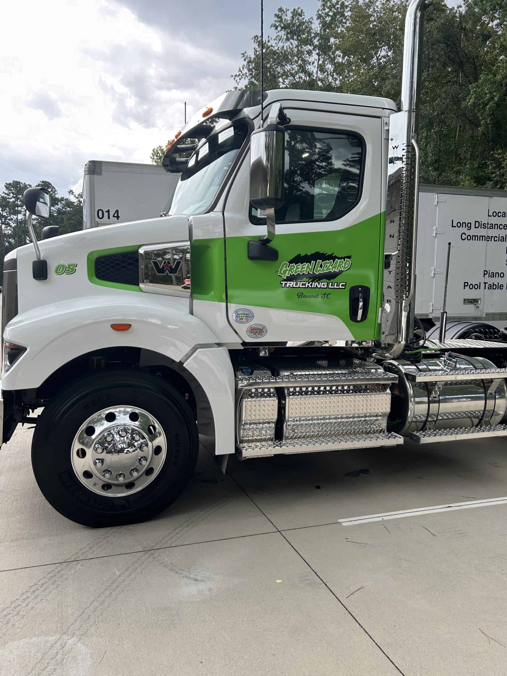 A white and green semi-truck cab is wrapped with Green Lizard Trucking branding in a lot.
