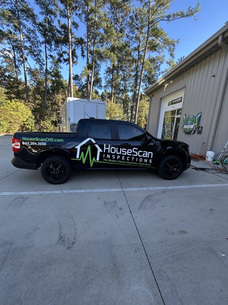 A black pickup truck wrapped with HouseScan Inspections branding parked by the shop.