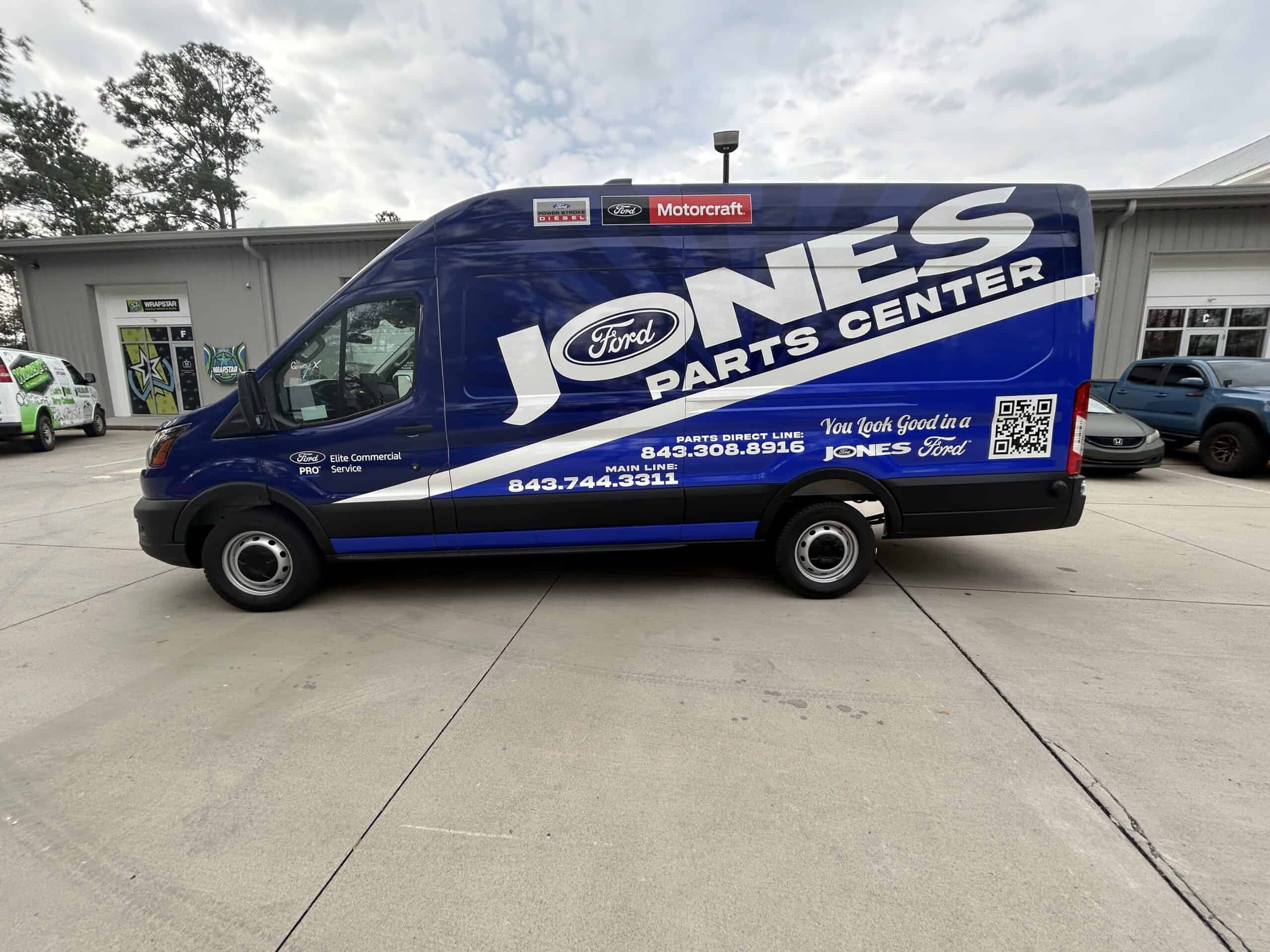 A blue Ford Transit van wrapped in Jones Ford Parts Center branding parked outside the shop.