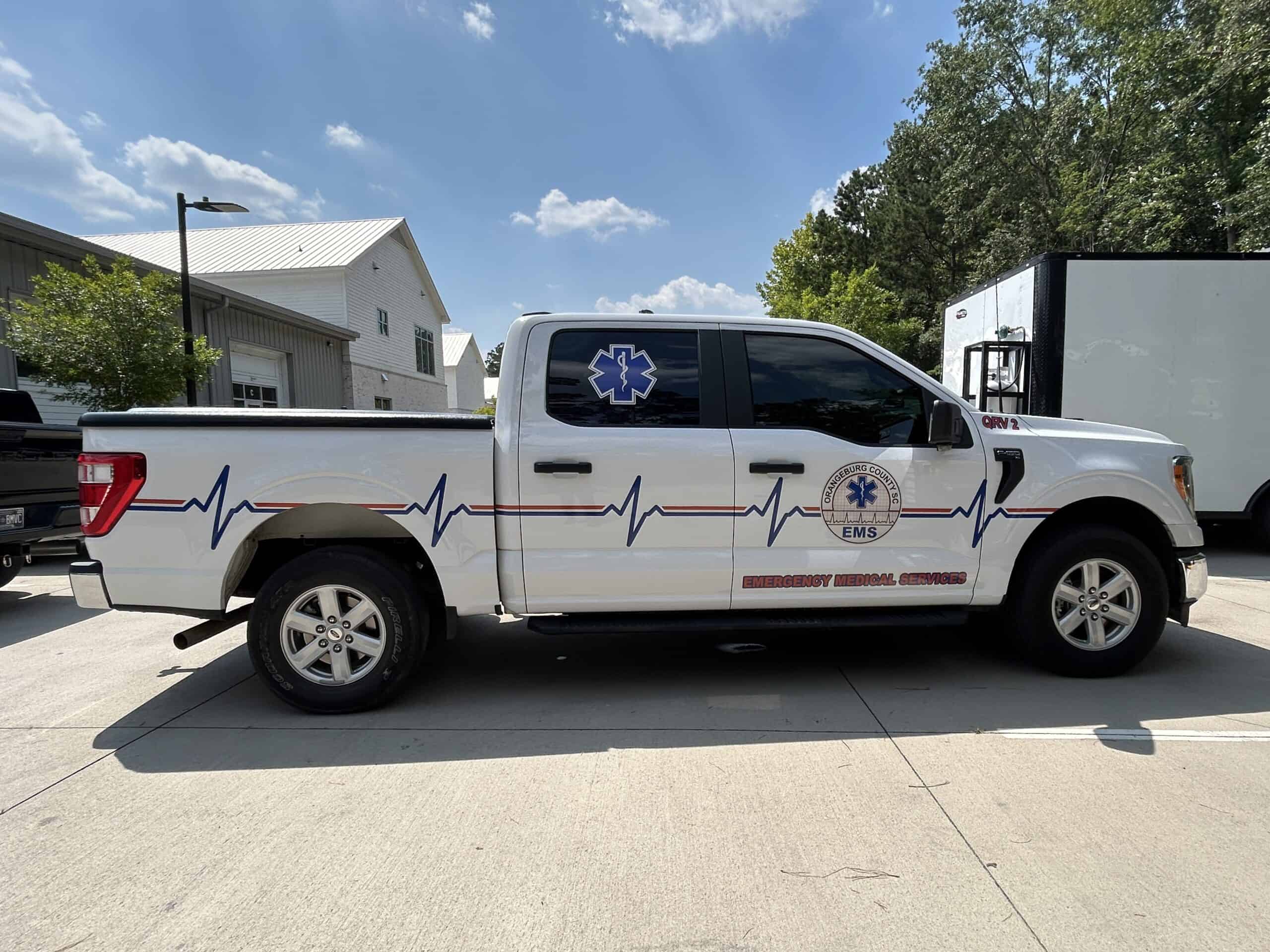 A white Ford pickup wrapped with Orangeburg County EMS branding and a heartbeat line graphic.