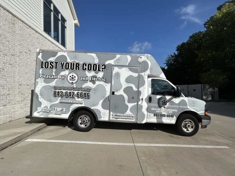 A white service van with a gray camouflage wrap for Pleasant Air and Electric sits outside an office.