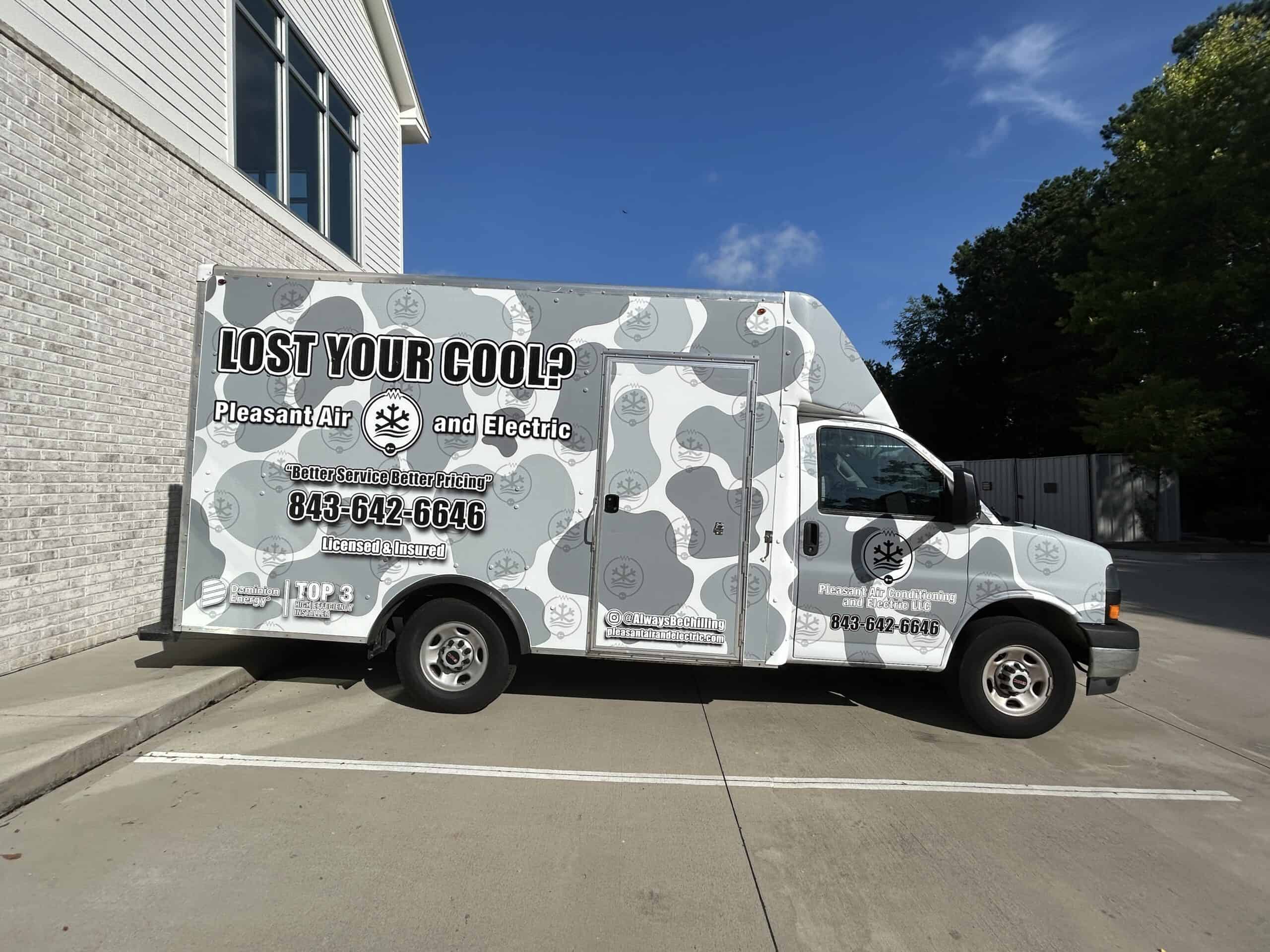 A white service van with a gray camouflage wrap for Pleasant Air and Electric sits outside an office.