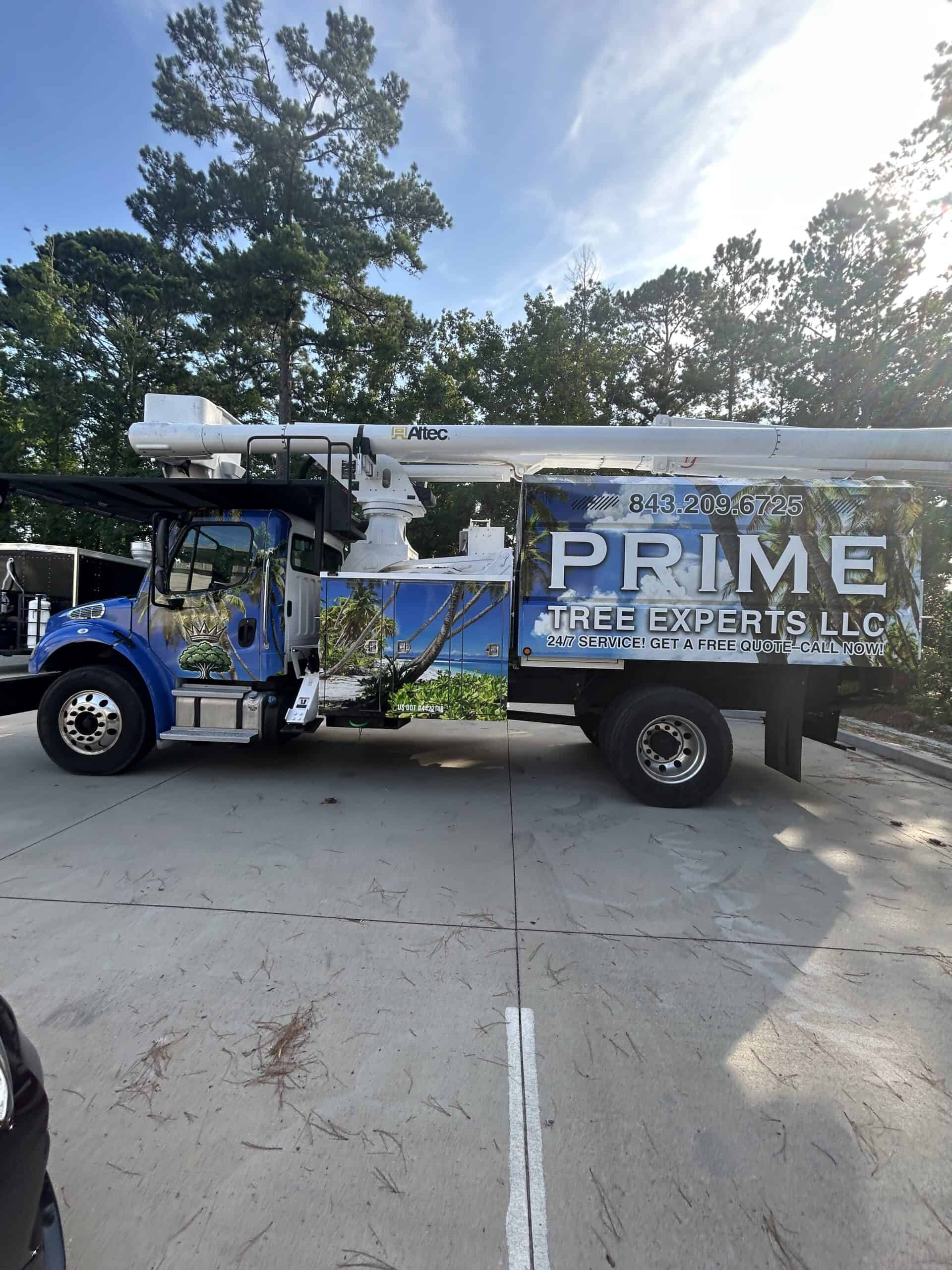 A blue bucket truck wrapped in branding for Prime Tree Experts parked with its boom folded down.